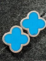 Close-up of one earring showing blue quatrefoil front and silver edge