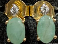Front view of both stud earrings showing emerald cabochons and accent stones