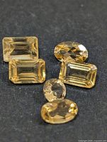 Five loose citrine gemstones on dark background showing shapes and color