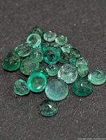 pile of small faceted emeralds on dark surface