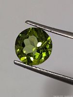 Front view of round faceted green peridot held by tweezers