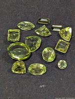 Close view of 14 faceted peridot stones on dark background