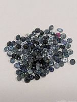 Pile of small round faceted sapphires in varying blue tones and one pink