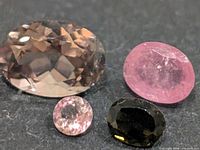 Four loose faceted tourmaline stones arranged on dark surface