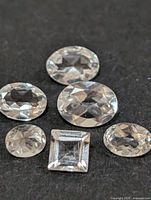 Six loose faceted white topaz gemstones of various cuts on black background