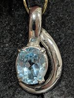Front view of silver pendant showing blue topaz and swirl design