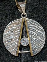 front view of circular silver pendant with CZ and gold-tone accents