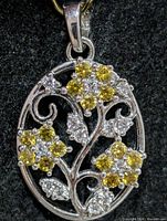 Front view of oval silver pendant with yellow and clear CZ floral design