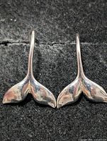 Front view of both silver whale-tail earrings on dark fabric