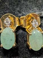 Front view of both stud earrings showing emerald cabochons and diamond accents