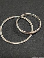 Two polished silver band rings on dark background