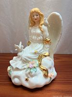 Front three-quarter view of porcelain angel music box on cloud with doves and flowers