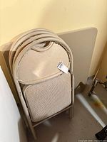 Stack of four beige metal folding chairs and folded beige metal card table
