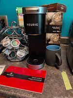 Coffee brewer with pod holder, mug, cleaning cup and boxes visible