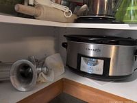 Shelf showing Crock-Pot digital slow cooker and manual meat grinder with funnel attachment