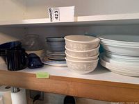 Overview of shelf showing Corelle bowls, dinner plates and cobalt glass pieces