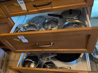 Open drawers showing assortment of stainless cookware, lids, cast iron pan