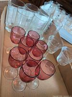 Box containing ruby aperitif stems in foreground, clear Cornflower tumblers and coupes in background