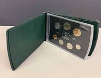 Interior view showing all seven coins and central medallion in acrylic lens inside green case