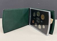 Open green leatherette folio showing seven-coin specimen set in plastic holder