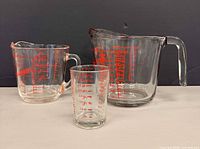 Three measuring vessels grouped: 1-litre cup, 2-cup cup, 30 ml shot glass