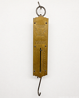 Full view of brass spring balance scale hanging by ring showing hook and body