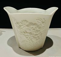 Front view of white bisque porcelain vase showing floral relief and scalloped rim