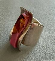 Profile view of ring showing wide silver band and wavy amber-coral inlay