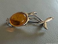 Front view of silver fish brooch highlighting amber cabochon and overall design