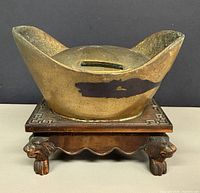 Front view of brass sycee coin bank on wooden lion-mask stand