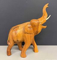 Full view left side of carved wood elephant figurine showing raised trunk and tusks