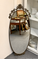 Front view of oval brass framed mirror leaning against wall