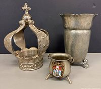 Front view of the three metal items: Santo crown, hammered vase, tripod pot