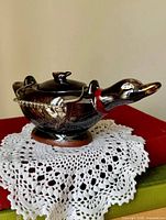 Profile view of duck-shaped sugar bowl on doily
