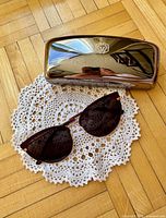 Sunglasses laid on doily beside metallic Kivuli case