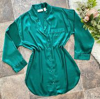 Front view of emerald green satin sleep shirt laid flat showing buttons, collar and pocket