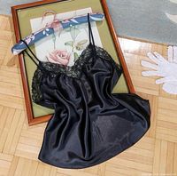 Full view of black satin camisole laid flat showing front, lace neckline and straps