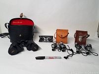 Lot of four vintage optical viewing devices including binoculars and opera glasses displayed with cases and a marker for scale.