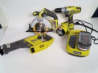 Five Ryobi power tools and charger arranged on white surface: P250 drill, P503 circular saw, P513 reciprocating saw, P703 flashlight, P104 battery on charger.
