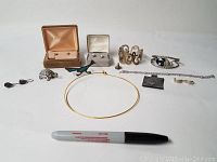 Full view of all jewelry items arranged in a row with a black marker for scale showing earrings, bracelets, pins, necklace, and charm.