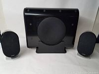 Front view of two Paradigm Millennia CT Shift speakers flanking one subwoofer, all black with a compact design and silver stands on the speakers.