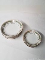 Two stacks of white china bowls with a green and gold Alberta decorative pattern around the rim, larger 7.5 inch bowls stacked on left, smaller 5.5 inch bowls stacked on right