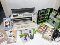 Overall view showing machine, cartridges, case, blade, overlay, power adapter, and markers laid out