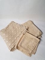 Vintage lace tablecloth and two coordinating napkins folded and displayed together showing fabric texture and color.