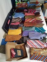 Lot of 71 men's neckties arranged on a table, some in original boxes or new with tags, showing varied patterns and colors.
