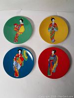 Four Pier 1 stoneware decorative plates from the Geisha collection, each on a different solid color background (green, yellow, blue, red) featuring a geisha illustration.