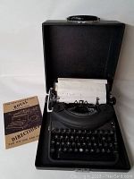 Photo of the Underwood Royal Noiseless 77 typewriter in its open black carrying case with instruction pamphlet beside it.