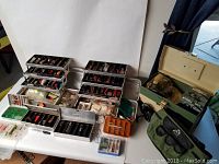 Fishing tackle boxes open displaying numerous old fishing lures, baits, hooks, and accessories in trays and small boxes.