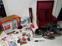 Full lot overview showing toolbox, irons, sewing machine, box, patterns, pin cushion, and wooden shoe tool.