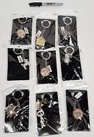 Nine new Alexander Kalifano keychains in original packaging displaying a variety of designs including teapots, turtles, a poodle, a heart, a cuckoo clock and a key.